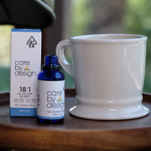 Photo of Care By Design 18:1 sublingual drops on a table aside a tea cup