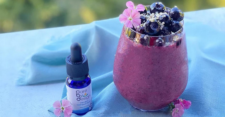 Photo of a blueberry smoothie beside a dropper bottle of Care By Design CBD drops