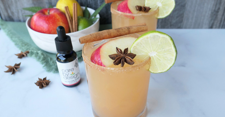 Photo of Spiced Apple CBD Margarita on a table beside a bowl of fruit and a Care By Design tincture bottle