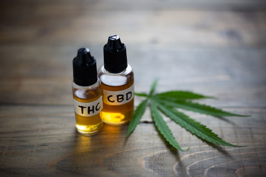 Photo of two small bottles, once containing THC oil and the other CBD oil sitting on a table beside a fresh cannabis leaf