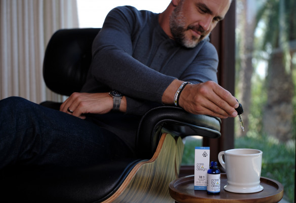 Photo of seated man adding a dropper full of Care By Design tincture into a cup of tea