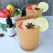 Photo of Spiced Apple CBD Margarita on a table beside a bowl of fruit and a Care By Design tincture bottle